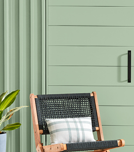 Black woven and wood chair against a Green Trellis shed — a light, calming green.