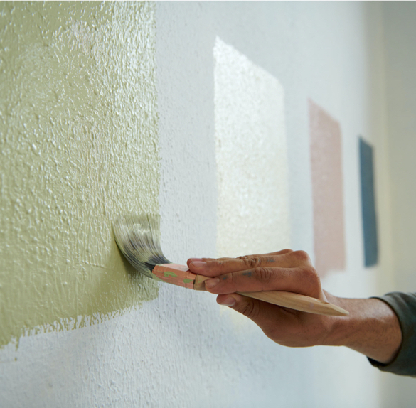 Hand painting a color square to a wall with three other color squares in the background.