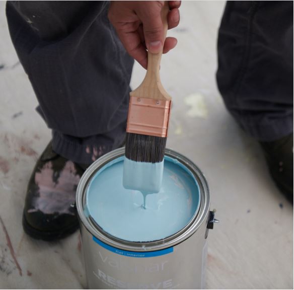 Hand pulling a brush out of a can with paint dripping off the brush.