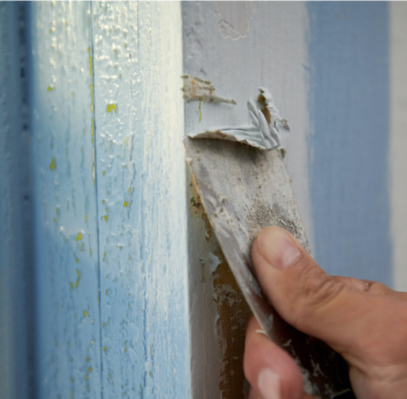 Close-up shot of hand using a scraper to remove paint from a wall.