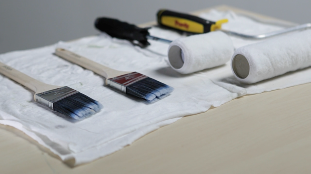 White rag on surface upon which rest two brushes and two rollers.