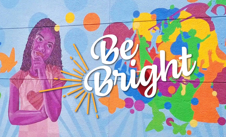 Colorful mural features purple-toned child contemplating splashes of bright colors with words, “Be Bright.”