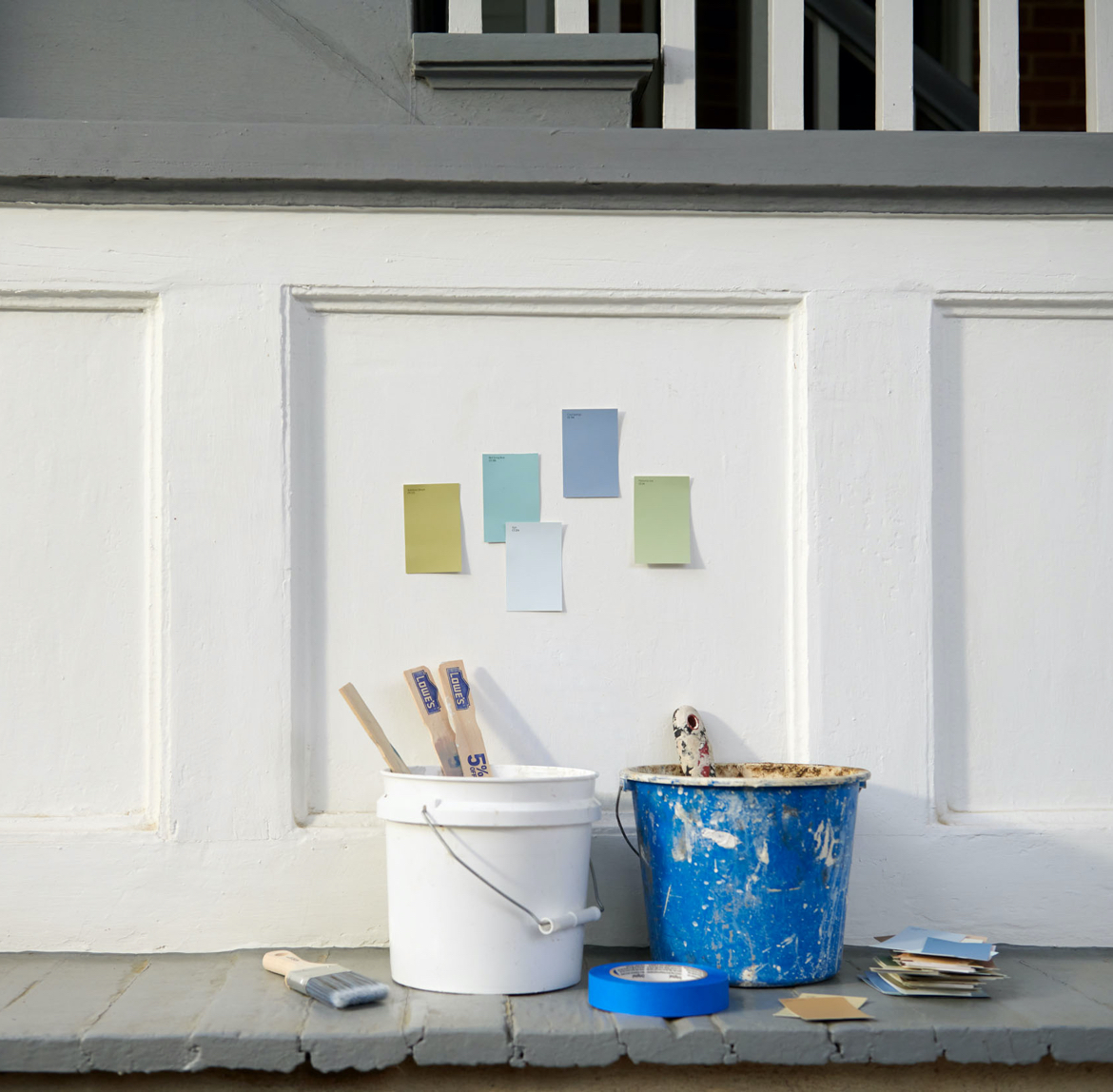 White, paneled wall beneath stairs with color chips. Messy paint pails with paint stirrers and chips below.
