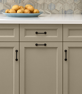 Close-up of  Ivory Brown (a washed brown)  kitchen cabinets with lemons on a plate resting on white counter.