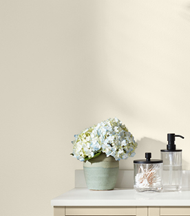Hydrangeas, cotton swabs in a glass jar and soap pump on bathroom counter corner against Cozy White walls.