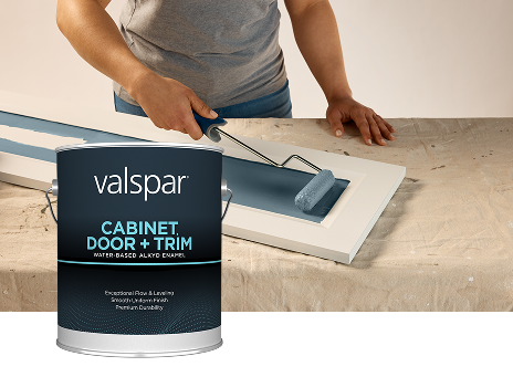 Valspar Cabinet, Door + Trim Oil-Enriched Enamel can shown alongside a paint roller applying Cottage Door blue-gray paint to cabinetry, highlighting a smooth, durable finish for detailed interior projects.
