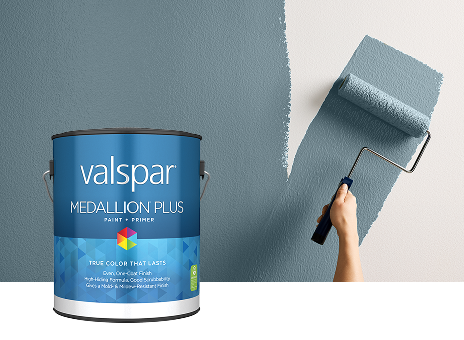 Valspar Medallion Plus Interior Paint + Primer can displayed beside a paint roller applying a smooth coat of Cottage Door blue-gray paint to an interior wall, showcasing rich color coverage and a refined finish.