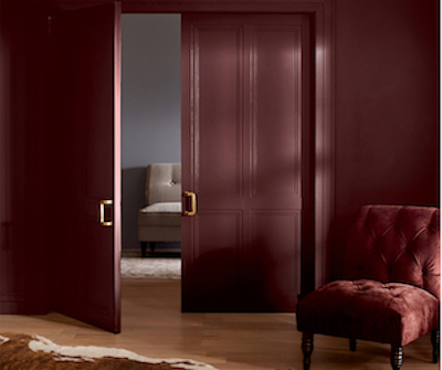 Tall, paneled doors and upholstered chair in deep monochromatic warm red, slightly ajar to next room.