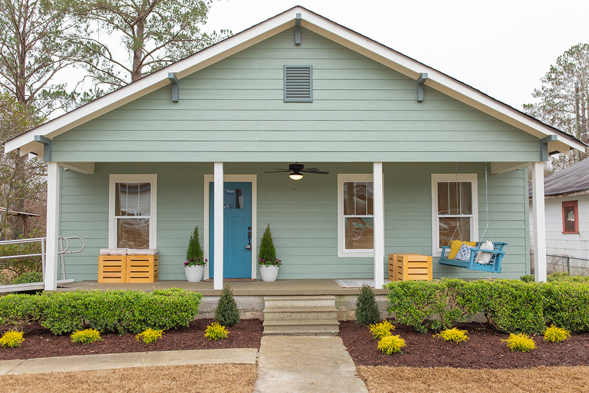 Light-green house with blue door, squared columns and a blue porch swing.