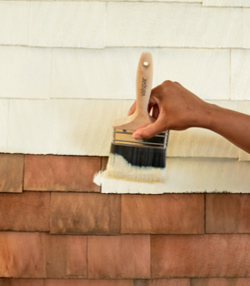 Hand with brush painting wooden shingles in a soft neutral.