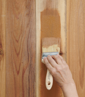 Hand with brush staining a wood panel.