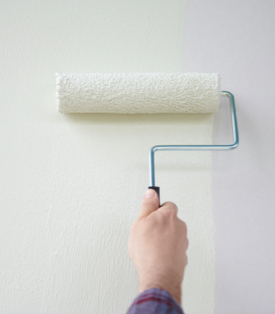 Hand holding a roller and painting a white wall.