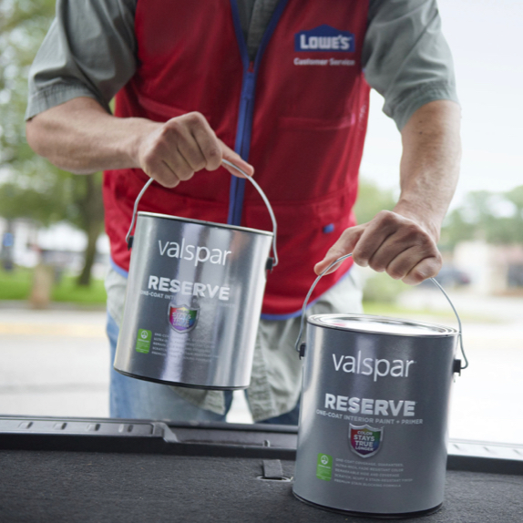 Lowe's® customer service representative in red vest, loading two cans of Valspar® Reserve® paint into back of car.