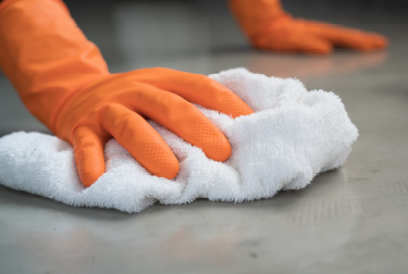 Gloved hand with rag wiping solution onto concrete floor.