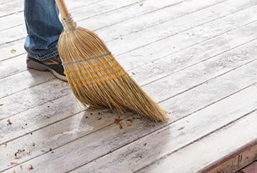 Person in jeans and sneakers sweeping wood surface with a broom.