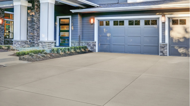 A suburban house that has an attached garage with a large concrete driveway in front of it.