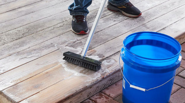 A man using a soapy brush mop to clean a wood deck surface.
