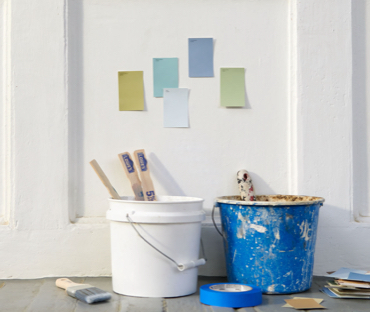 White and blue paint buckets, paint brush, blue tape and swatches on floor. Swatches on white wall. “Color Consultation.”