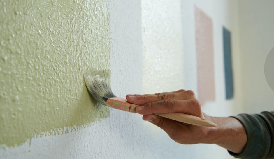 Painting wall green with brush. Color swatches on wall in background.