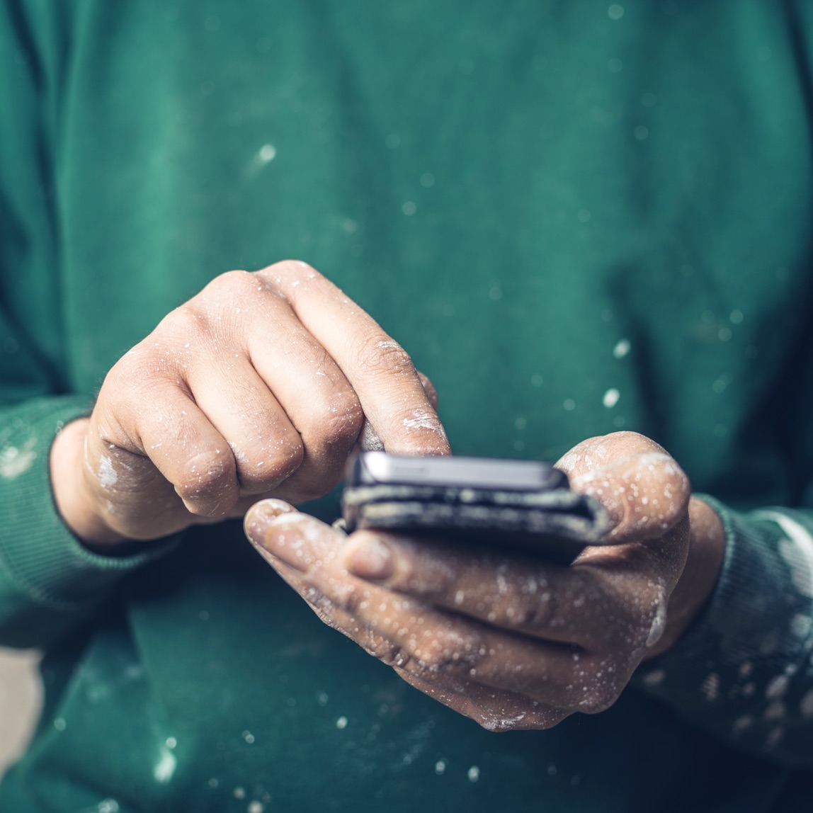 Imagen de manos cubiertas con salpicaduras de pintura usando un teléfono inteligente para buscar algo