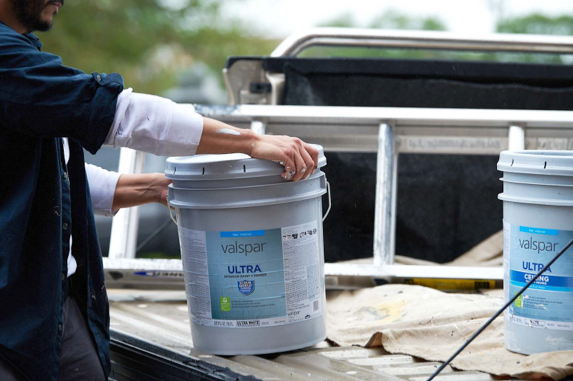 A bucket of paint being lifted off the back of a pickup truck with a second bucket and ladder in background.