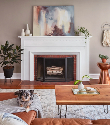 White fireplace against warm wall, copper table and planter and modern art canvas resting on mantle.