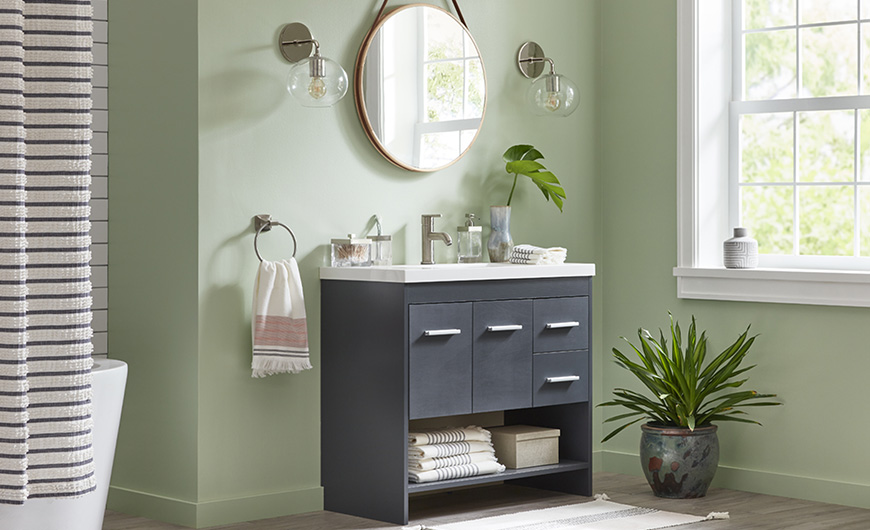 Dusty green bathroom with dark charcoal gray vanity, large window, plants and round mirror.