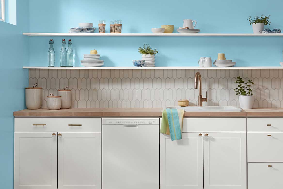 White lower kitchen cabinets with wood countertops, bright blue walls and open white-painted shelving.