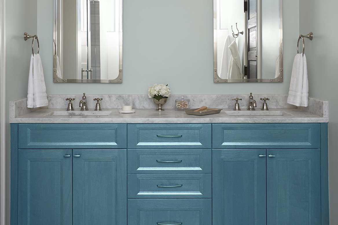Glossy, watery-blue bathroom cabinets below marble-top double sinks and double mirrors.