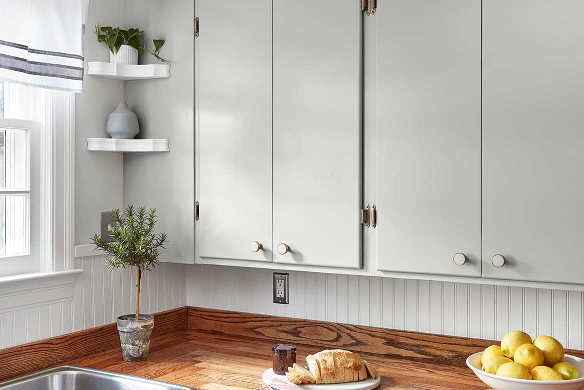 Tall, soft-gray kitchen cabinets with beadboard backsplash, wood countertops and raised bowl of lemons.