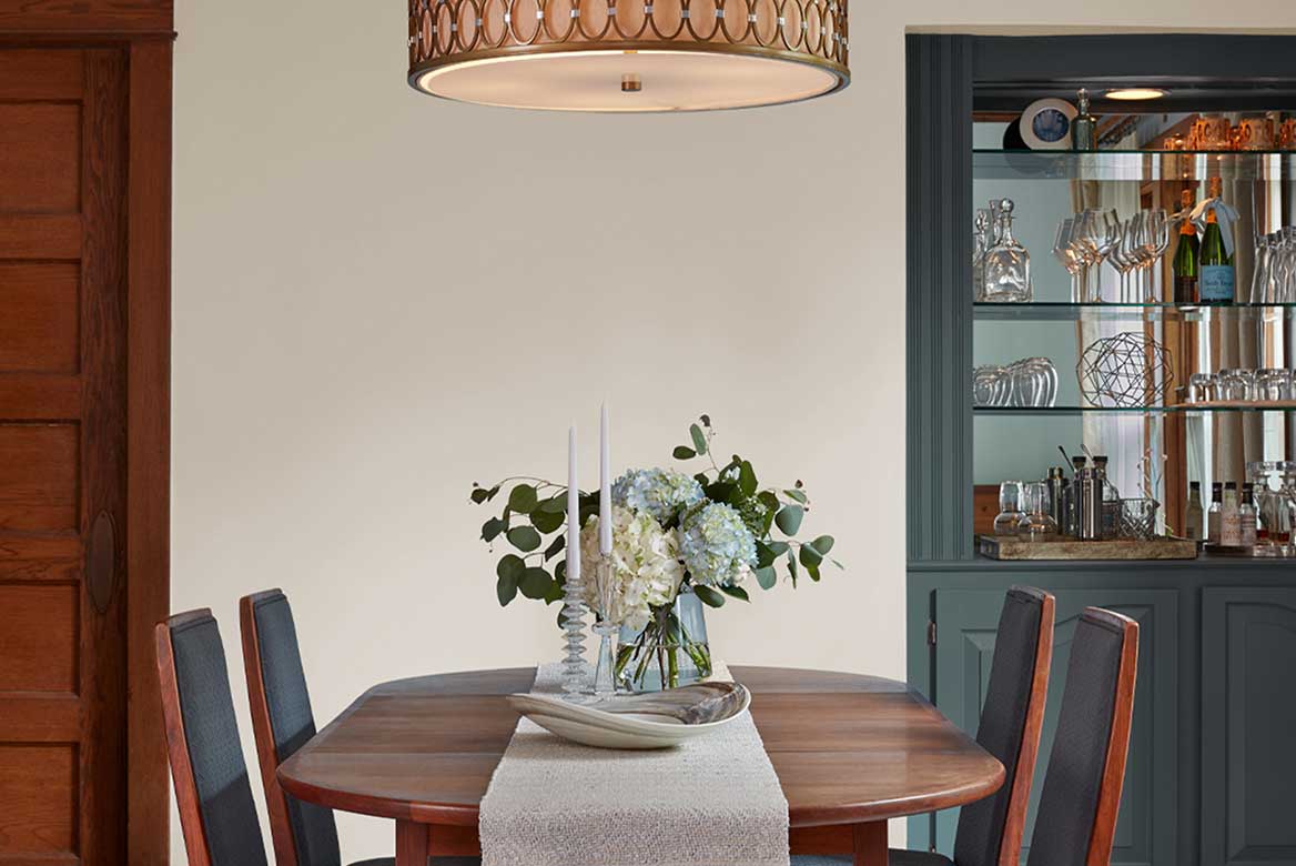 Dining room with built-in green hutch, soft gray walls, oval and wood dining table with fresh-cut hydrangeas. 