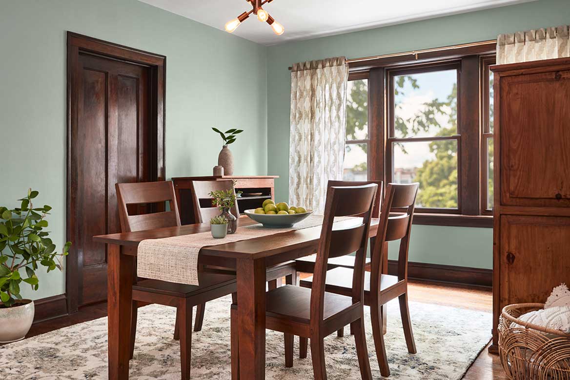 Dining room with calm green walls and darker wood furniture and décor, including table, door and window frames.