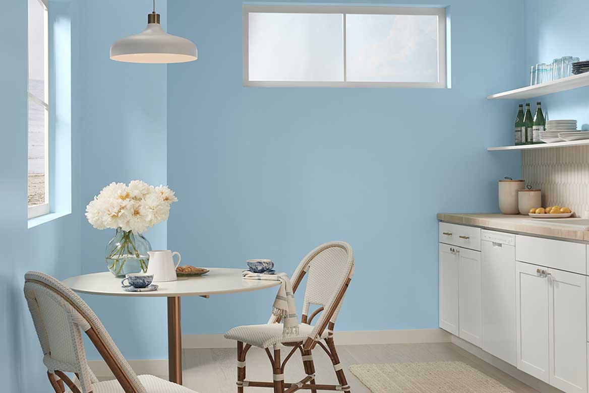Light blue kitchen corner with small bistro table set with coffee cups and fresh bouquet of white flowers.