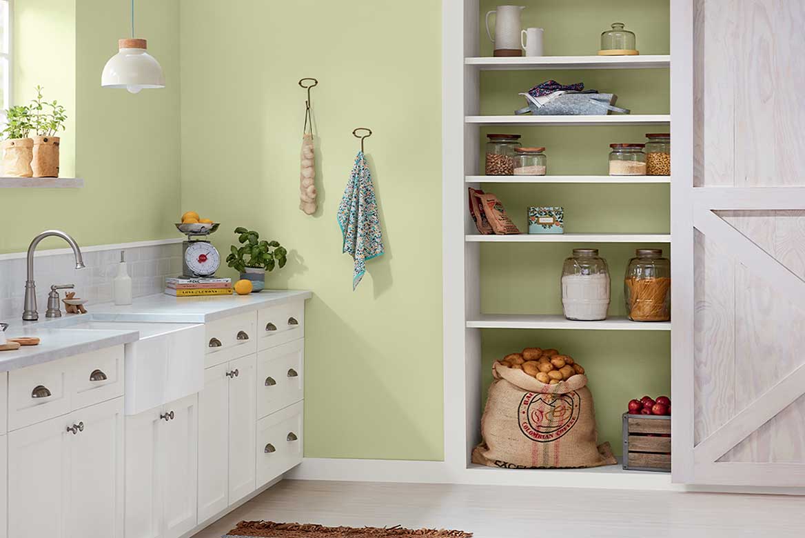 Bright green kitchen walls contrast with white cabinetry. Whitewashed barn door is open to reveal neat pantry.