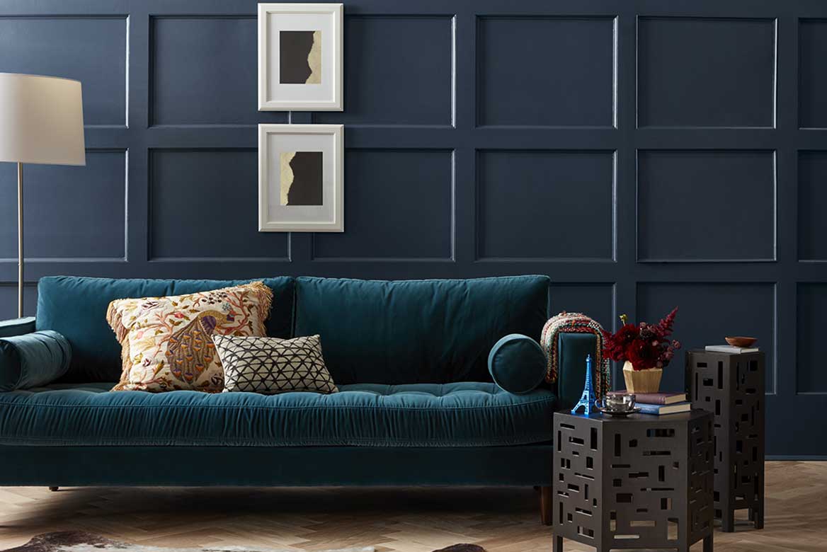 Dark, monochromatic coffered wall with deep-blue velvet upholstered couch and pair of geometric side tables.