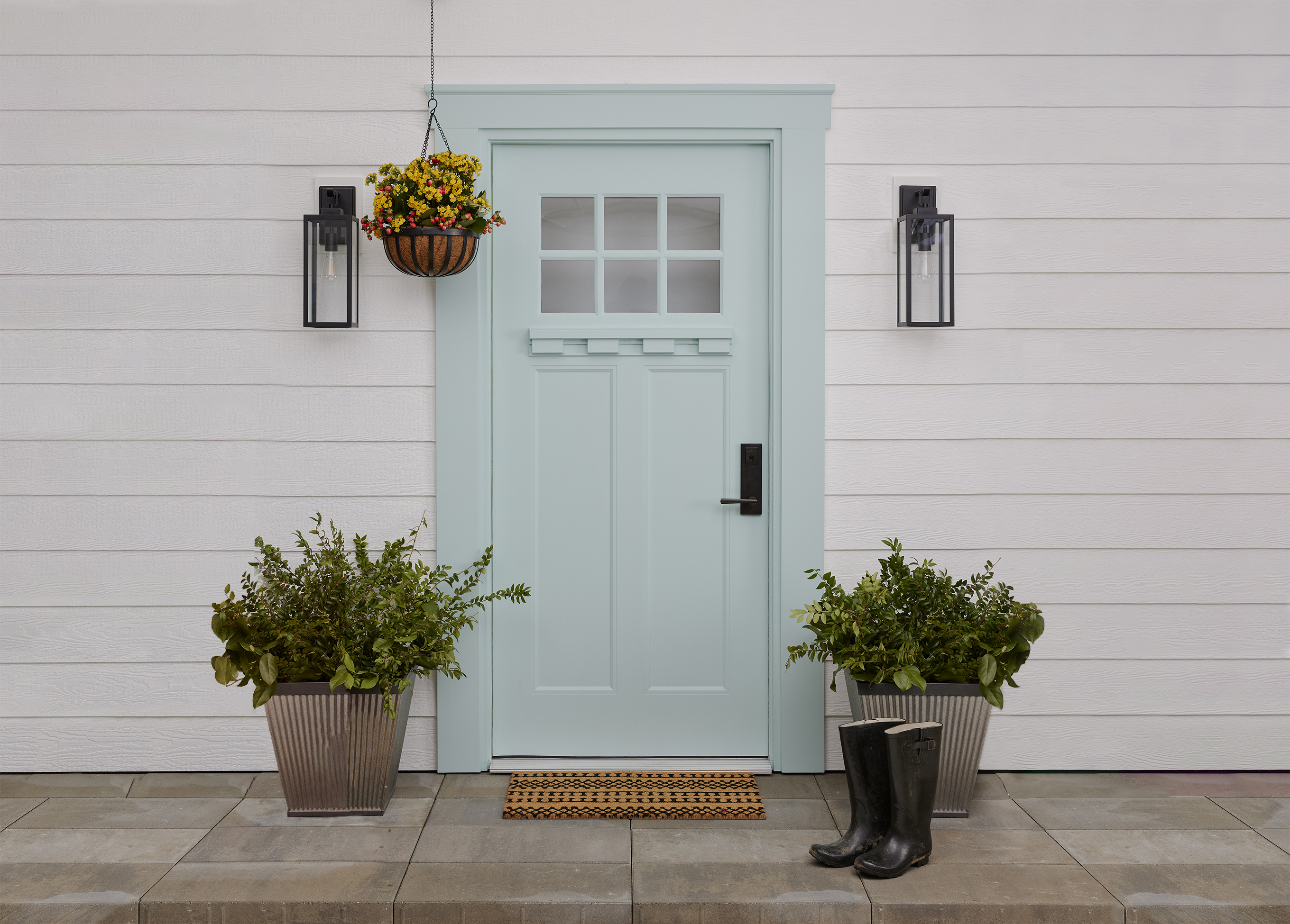 A light-blue door accessorized with rain boots, potted plants and a doormat. 