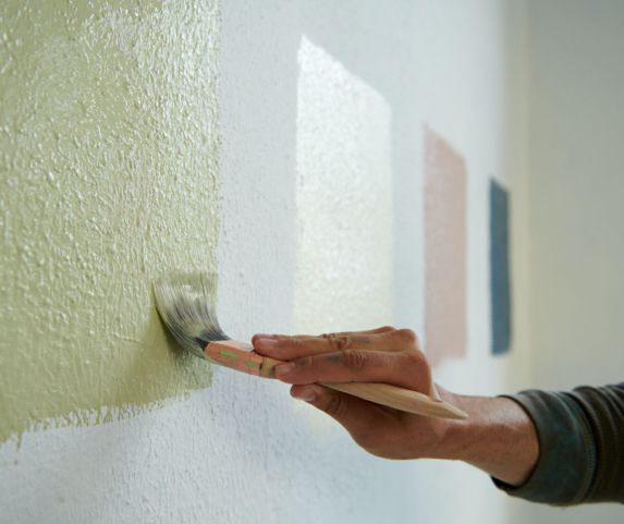 person painting multiple color swatches on wall to choose paint color 