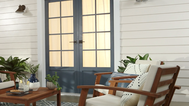 Porch with wooden lounge chairs, table and plant with grayish-blue French doors, white trim and light tan wall.