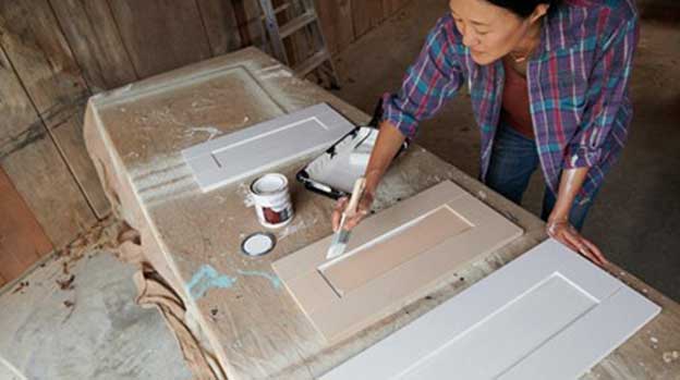 Painter priming wood vanity doors set on drop cloth-covered table.