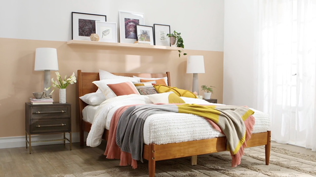 Pillow-covered bed against sandy neutral half wall accent color with matching shelf and modern side-table lamps.