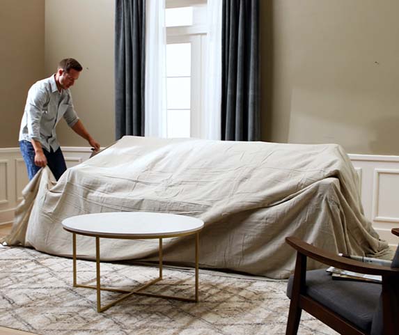 man covering couch with drop cloth