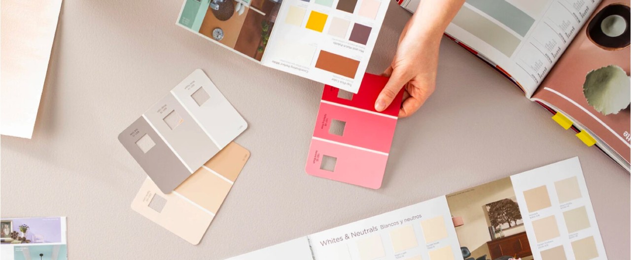 Hand holds color brochure and three-color palette paint chip in reds as if working with a client across the table.