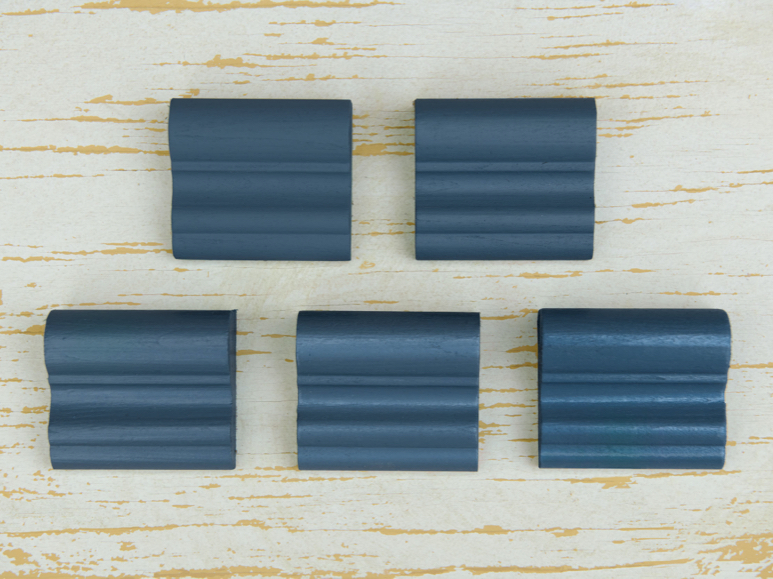 Five pieces of trim in different shades of blue on distressed wooden tabletop.