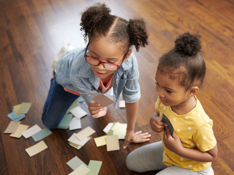 Two girls sitting on floor with handfuls of paint chips strewn across wood floor.
