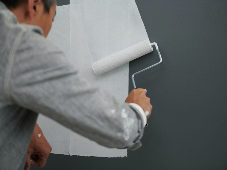 Person rolling white color over a dark gray wall.