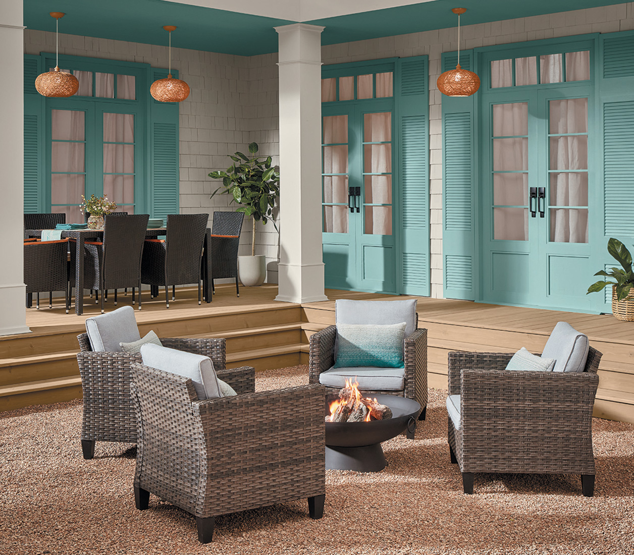 Deck stained with Prairie Path, wicker chairs around a fire pit, light fixtures and a dining room table in background.